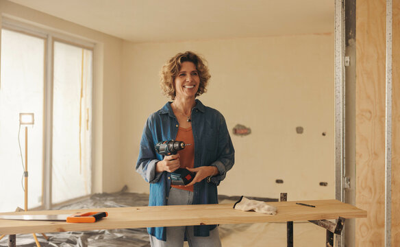 Fototapeta Woman holding a drill gun while renovating her home's kitchen