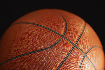 Orange basketball in the light on a black background, sports background