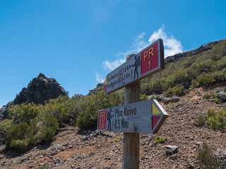 Tourist Signpost at hiking trail PR1.2 to Pico Ruivo - at 1,861 m the highest mountain and PR1 to Pico Areiro second highest peak, Madeira , Portugal. Blue sky, copy space - 766495197