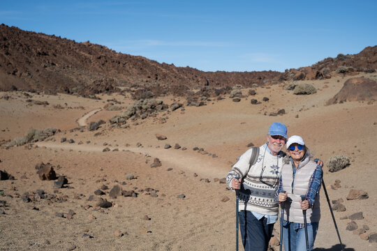 Active elderly retired couple with backpack walking outdoors with help of poles enjoying nature, freedom and free time. Arid terrain at the base of Teide volcano on the island of Tenerife