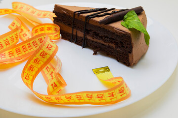 piece of a chocolate cake wrapped with a yellow measuring tape diet and healthy living concept image.