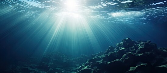 The sunlight is shining through the water in the ocean, creating a beautiful natural landscape with the sky and sun above and the underwater world below