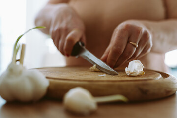cooking, slicing garlic cloves on wooden cutting board