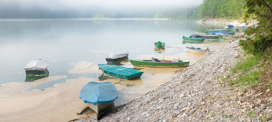 lake Sylvensteinsee with moored rowing boats at gravel beach, foggy day