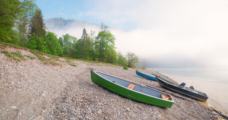 fog over lake Sylvensteinsee, gravel beach with boats, spring landscape upper bavaria