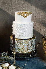 Gilded wedding cake with gilded decorations, white and beautiful against a loft wall.