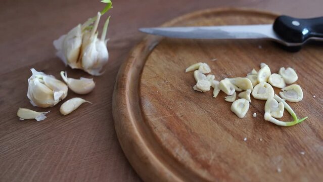 cooking, slicing garlic cloves on wooden cutting board