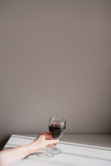 Minimalist aesthetic neutral background with woman hand holding red wine glass