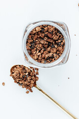 granola in a golden spoon next to a glass jar on a white background