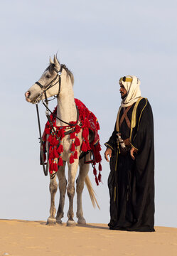 Man in traditional clothing in KSA with his horse in a desert