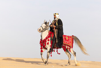 Saudi Man with his white stallion in a desert, shooting an arrow