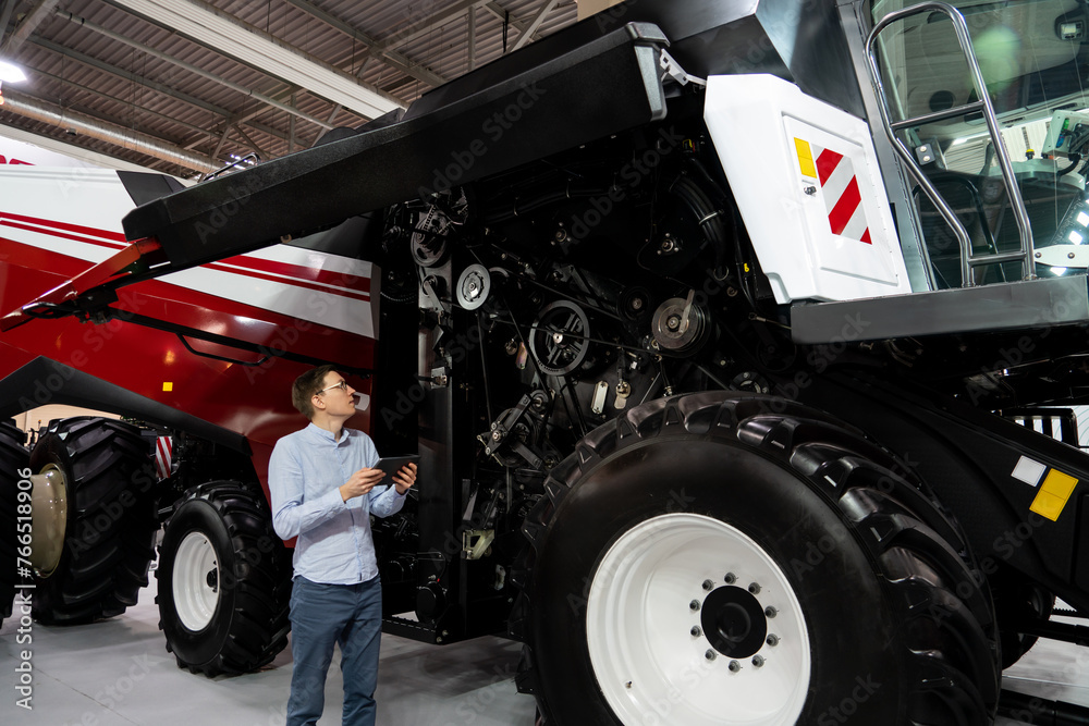 Poster Serviceman with digital tablet on a next to ombine harvester with open hood..