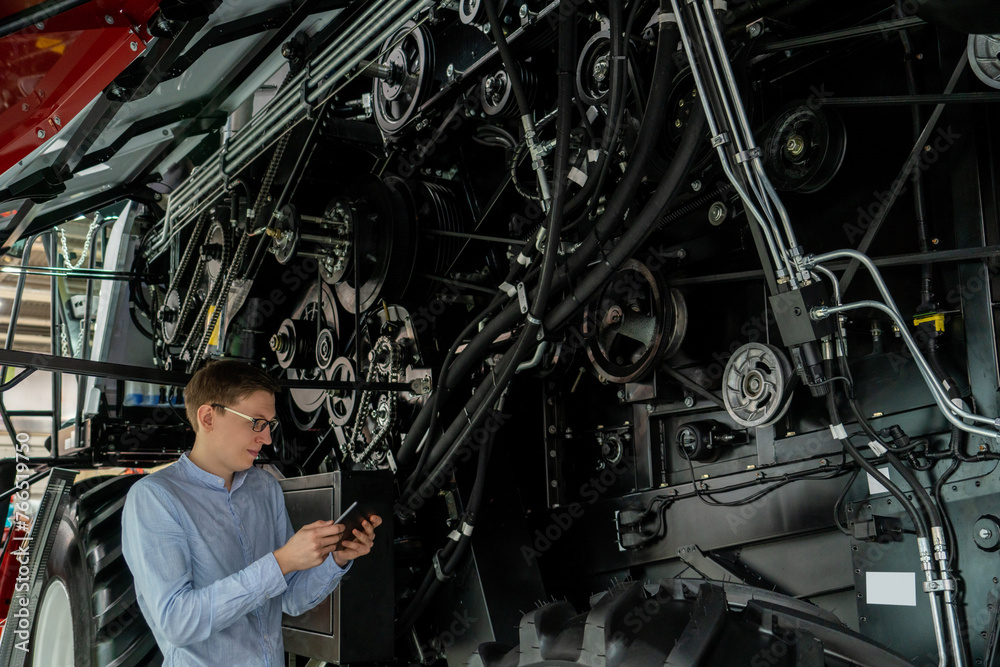 Poster Serviceman with digital tablet on a next to ombine harvester with open hood..