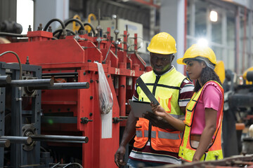 Manufacturing industrial concept. Male and female engineer workers working at manufacturing production lines in factory during manufacturing process, wearing safety uniform and use digital tablet