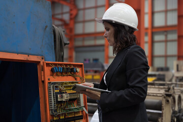 Female factory worker inspecting quality of electric system at production line conveyor in industry...