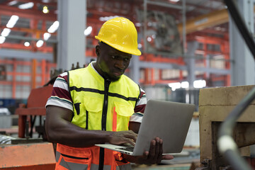 Male factory worker working with laptop computer in the industry factory. African American worker inspecting quality of manufacturing process in plant