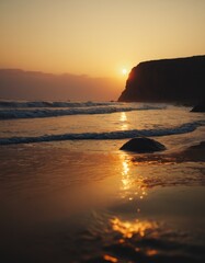 A serene sunset casts a golden glow over a tranquil beach, with waves gently lapping at the shore and a rock basking in the reflected light.