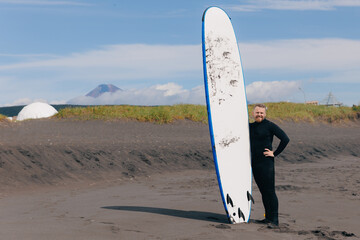Lifestyle Extreme Surfer man in wetsuit with surfboard on volcano of Kamchatka Russia, winter...