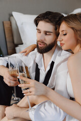 Joyful newlywed couple woman and man toasting with champagne in bed of hotel