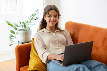 Happy young woman working on her laptop in living room interior