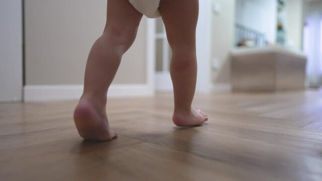 toddler taking their first steps at home. little one learns to walk independently. child learns to walk on floor with bare feet at home. baby first steps are a family joy. child walk first steps