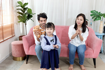 Happy Asian family. Chubby little girl daughter  playing with father and mother in living room. Parents spend time together with kid, show love to each other. Child with dad and mom relaxing at home.