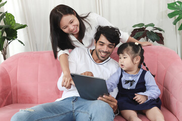 Happy family in living room, Chubby little girl daughter with her mother and father using tablet in living room. Kid spending online together with parents at home. Child, mom and dad in house.