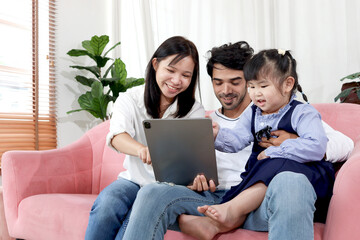 Fototapeta premium Happy family in living room, Chubby little girl daughter with her mother and father using tablet in living room. Kid spending online together with parents at home. Child, mom and dad in house.