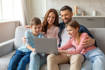 Cheerful young family with kids having fun with laptop at home