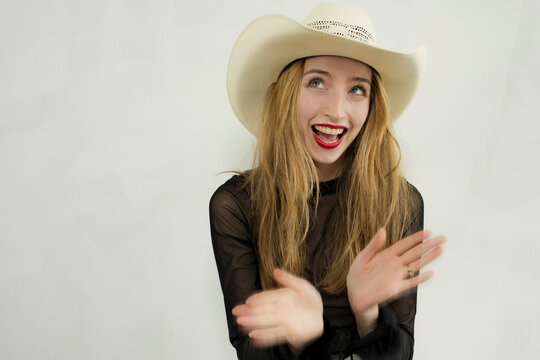Pretty young woman in white jeans, lacy black top and cowboy poses in a studio setting.