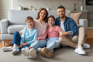 Smiling family with preteen kids sitting on floor in cozy living room