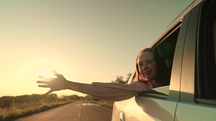 Smiling travel woman road trip riding car with hand in window at sunset sunrise enjoy freedom air...