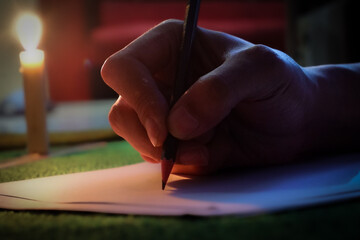 Close up of a man's hand writing on paper at night lit by candlelight, hand writing letter with...