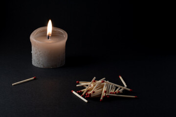 burning candle and matches on black background