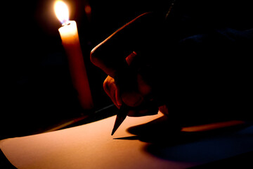 Close up of a man's hand writing on paper at night lit by candlelight, hand writing letter with...