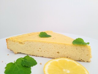 Piece of fit cheesecake with sliced lemon and melissa leaves.
