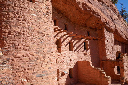 Red rocks of Manitou Springs cliff dwellings.  Natural adobe walls with stone and brick showing.  Ancestral Pueblo structures with ladders and railings showing access.