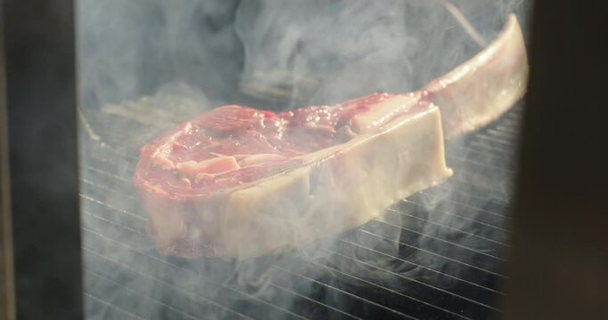 Roasting meat tomahawk steak on barbecue charcoal grill. Grilling BBQ meat. Smoke rising over juicy beef steak