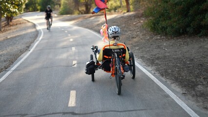 Rear view of elderly senior woman riding a recumbent electric bike on a bike path through a neighborhood in Southern California. Filmed in.