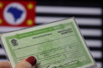 Brazil voter registration card in a woman’s hand with the São Paulo State flag in the background 