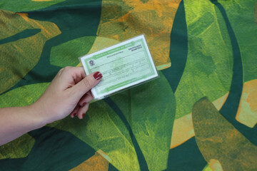 Brazil voter registration card in a woman’s hand isolated in a abstract green background  - obrazy, fototapety, plakaty