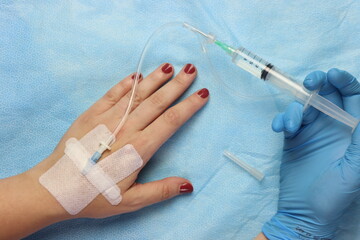 Syringe with drug connected with a peripheral catheter access in a woman’s hand  - obrazy, fototapety, plakaty