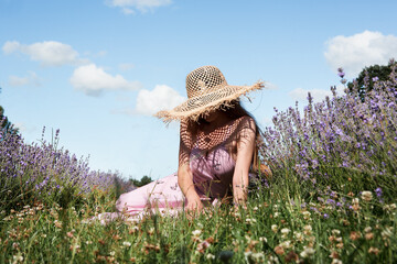Young sexy beautiful woman in a straw hat is sitting resting in a lavender field against the background of the sky.	