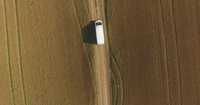 Aerial view of white truck driving along dirt road between two yellow agricultural fields with harvested crops