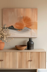 A wooden sideboard with light wood grain, a black vase and bowl on top, artwork hanging above the cabinet in the style of Scandinavian interior design, and neutral tones with soft orange accents.