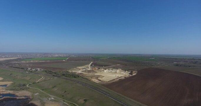 Drone panorama: One railway line along river and yellow spot of an open-pit sand quarry among black and green agricultural fields. Aerial view