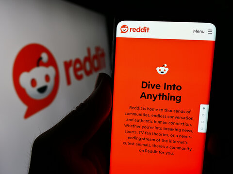Stuttgart, Germany - 03-15-2024: Person holding cellphone with webpage of US social media company Reddit Inc. in front of business logo. Focus on center of phone display.