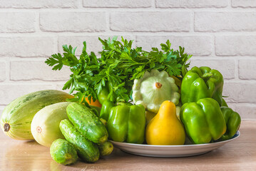 Heap of fresh green vegetables (parsley, cucumber, bell pepper, zucchini, cabbage) on a kitchen table; copy space; vegan and healthy eating concept
