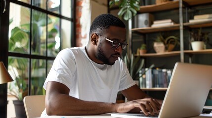 Fototapeta na wymiar An African American man wearing a white T-shirt is using a laptop.