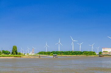 Landscape of Scheldt river and Linkeroever Left bank of Antwerp with Windmill farm wind power plant turbines on horizon, Antwerpen port area, Flemish Region, Belgium